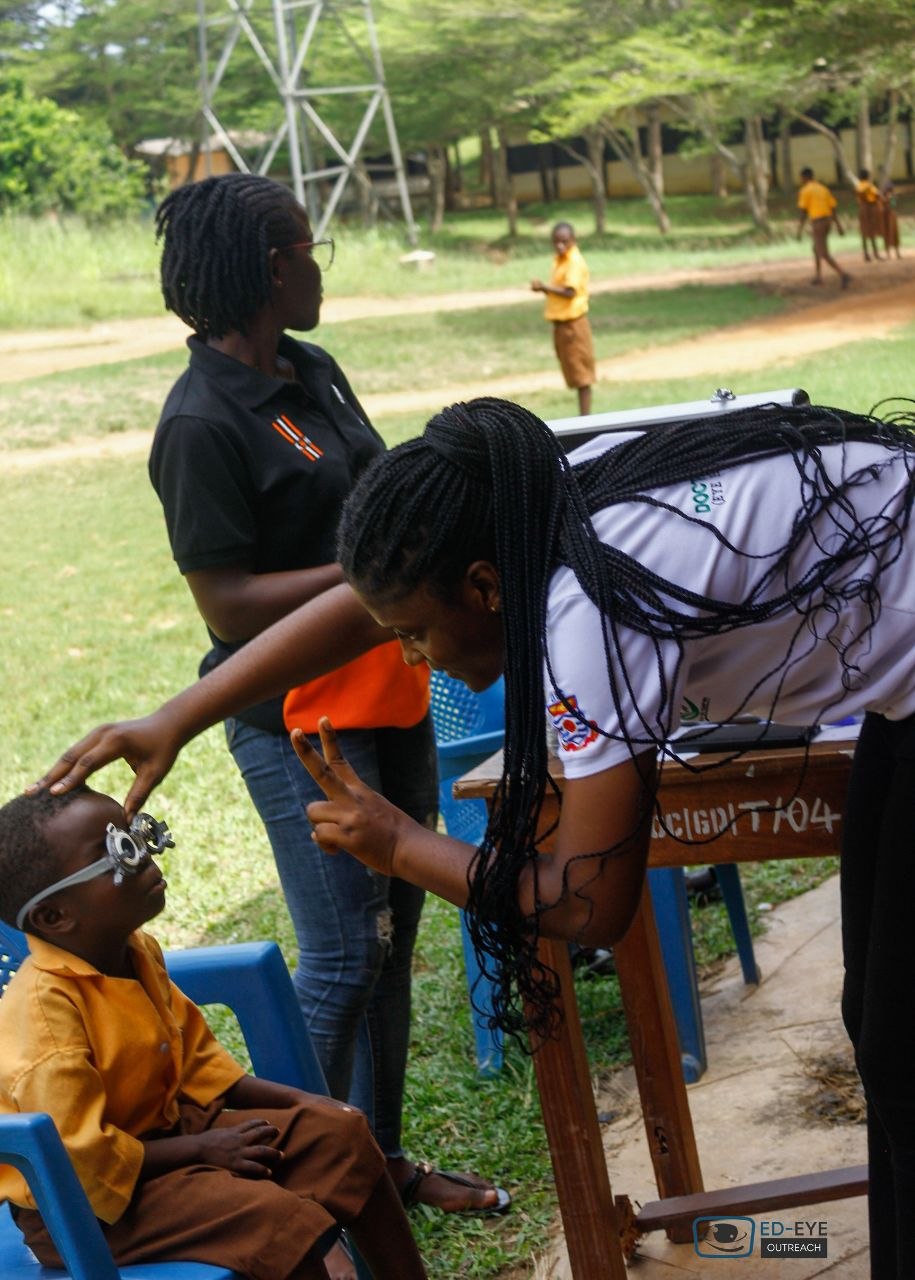 Volunteer assessing a student's vision outdoors with trial frames