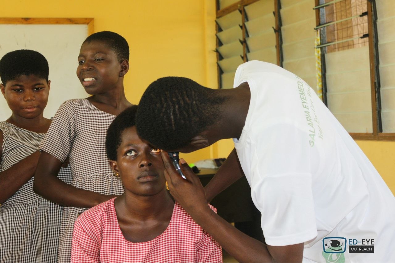 Eye-care volunteer examining a student's eye in a classroom
